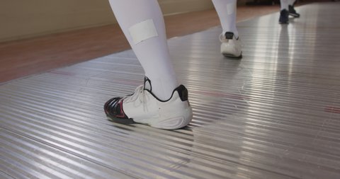 Close up low section of a two fencer athletes during a fencing training in a gym, sparring in fencing duel wearing sports shoes, jumping taking aim at each other in slow motion