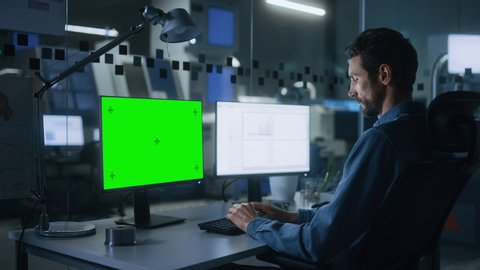 Engineer Works on a Computer, Two Monitor Screens Show Chroma Key / Green Screen and Spreadsheet Software Display. Modern High-Tech Industry 4.0 Electronics Production Factory