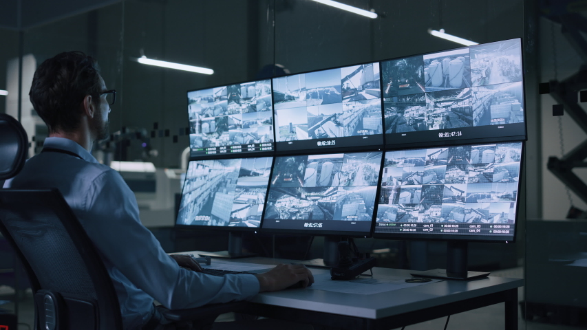 Industry 4.0 Modern Factory: Security Operator Controls Proper Functioning of Workshop Production Line, Uses Computer with Screens Showing Surveillance Camera Footage Feed. High-Tech Security | Shutterstock HD Video #1047398701