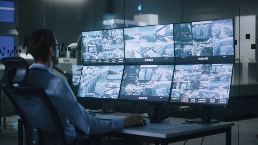 Industry 4.0 Modern Factory: Security Operator Controls Proper Functioning of Workshop Production Line, Uses Computer with Screens Showing Surveillance Camera Footage Feed. High-Tech Security | Shutterstock HD Video #1047398707