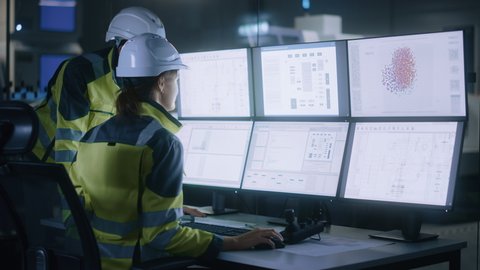 Industry 4.0 Modern Factory: Project Engineer Talks to Female Operator who Controls Facility Production Line, Uses Computer with Screens Showing AI, Machine Learning Enhanced Assembly Process