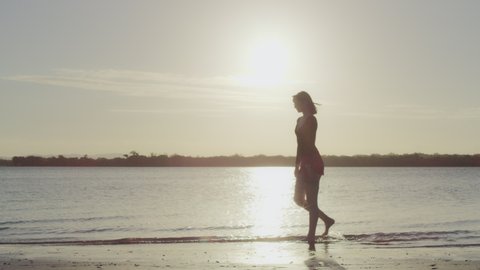 Woman model walking on a beach in silhouette with lake in the background in Australia.Wide shot on 4k RED camera.