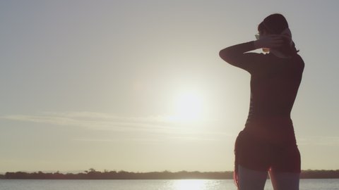Pan across woman model standing on a beach in silhouette with lake in the background in Australia.Medium close shot on 4k RED camera.