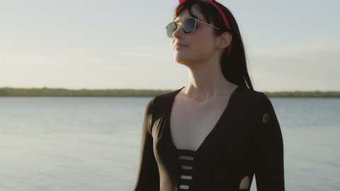 Young woman model walking along shore in red dress with lake in the background in Australia. Medium close on 4k RED camera.