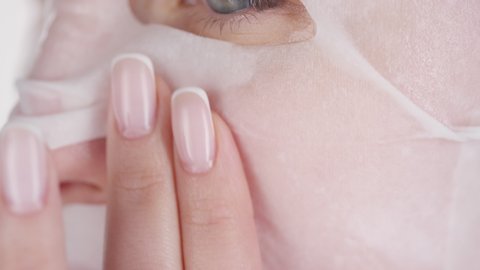 Extreme close up shot of young woman wearing sheet mask gently rubbing her face with her fingers