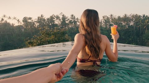 travel couple holding hands woman leading boyfriend in swimming pool enjoying luxury honeymoon on exotic vacation at hotel spa with view of tropical jungle at sunrise