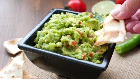 Hand dipping a nacho chip into a bowl of freshly made guacamole.