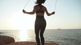 Young adult sporty woman training outdoors near sea jumping rope.  Slow motion footage.