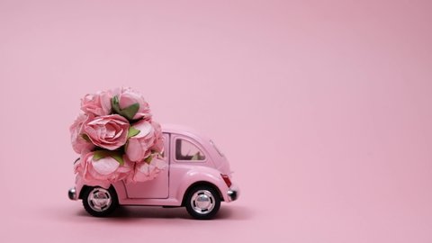 Omsk, Russia - December 20, 2018: Pink retro toy car delivering bouquet of roses on pink background. February 14 card, Valentine's day. 8 March, International Happy Women's Day