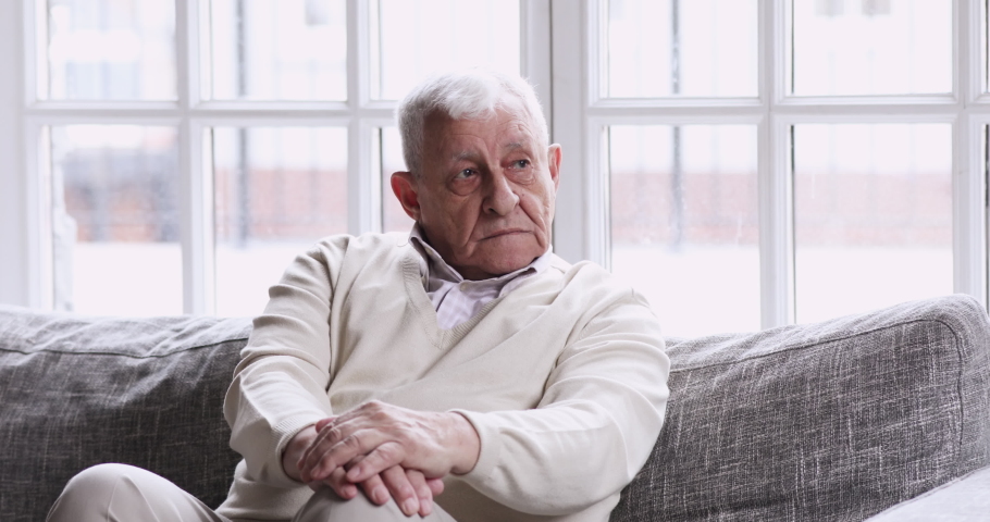 Pensive lonely older adult grandfather sitting alone on couch looking away lost in thought. sad thoughtful senior elder 80 years old man thinking of solitude feel melancholic upset suffer from Royalty-Free Stock Footage #1047422575