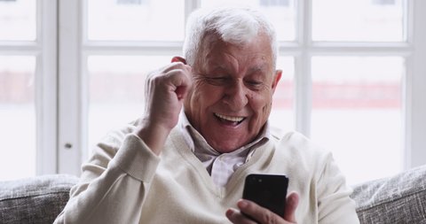 Overjoyed senior old 80s man hold phone look at screen excited about mobile app sport bet bid win concept. happy elder grandfather winner celebrate victory success read good news in cell text message.