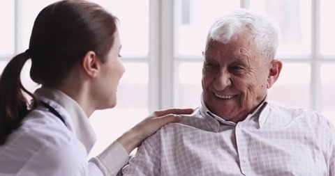 Smiling healthy senior elderly grandpa talk to caring young female doctor physician examining aged patient in hospital during medical checkup visit, eldercare treatment, old people healthcare concept.