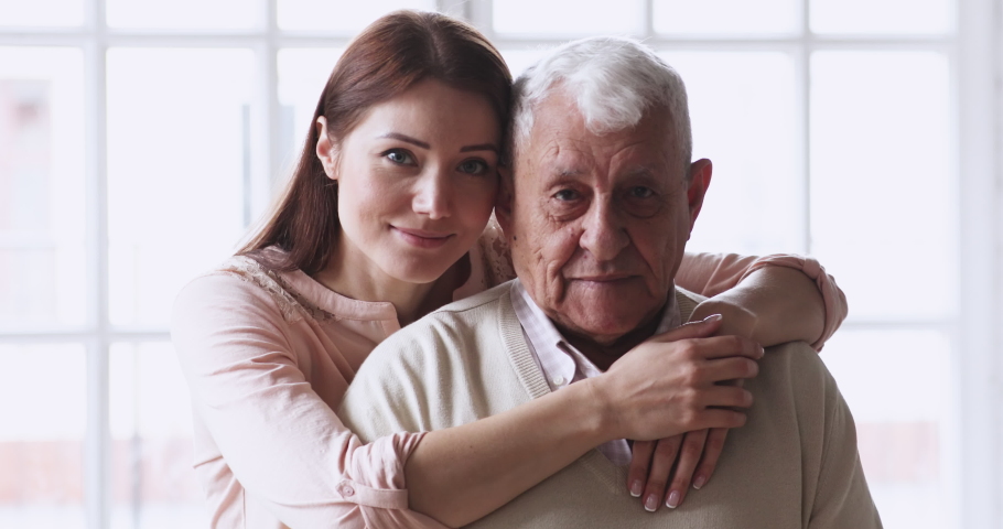 Happy caring grown granddaughter hug senior grandad cuddle look at camera. friendly 2 two age generations family old grandparent father and young adult grandchild daughter posing for close up portrait Royalty-Free Stock Footage #1047422596