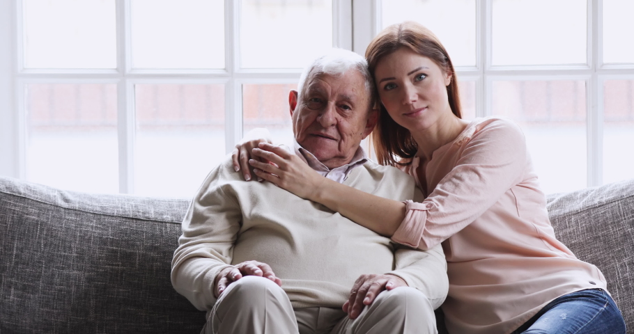 Happy young granddaughter embrace old grandfather sit on sofa. Loving smiling 2 two generations family grown daughter grandkid and senior grandpa elder father hug look at camera relax at home Royalty-Free Stock Footage #1047422605