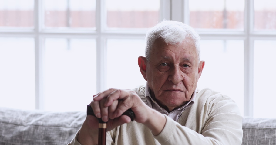 Happy older senior adult man hold cane sit on sofa looking at camera. relaxed optimistic disabled retired elderly 80s grandfather dental smile posing with walking stick at nursing home, portrait | Shutterstock HD Video #1047422638