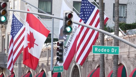 World famous Rodeo Drive Street Road Sign in Beverly Hills against American Unated States flag. Los Angeles, California, USA. Rich wealthy life consumerism, Luxury brands, high-class stores concept