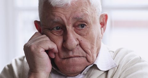 Worried thoughtful senior old adult 80s man sit alone at home thinking of lonely life. upset elderly gray-haired grandpa look away feel sorrow anxiety concept, close up old grandparent sad face view.