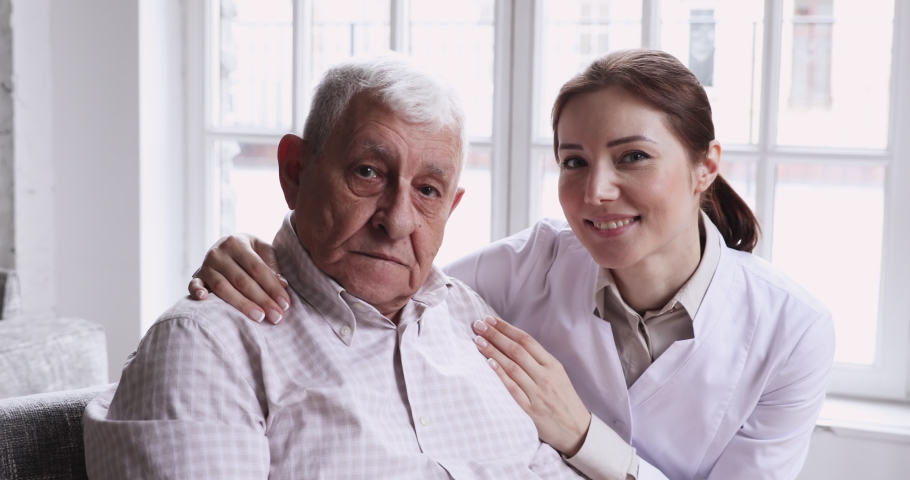 Caring smiling female caregiver embracing happy senior patient looking at camera. Young carer or nurse helping old elder care grandpa at nursing home, geriatric medical support concept, closeup Royalty-Free Stock Footage #1047425131
