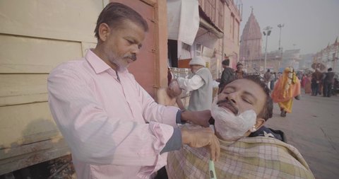 JANUARY INDIA 2020: Men shaving beard of his customer in outdoor street saloon for cheaper cost in Varanasi, Uttar Pradesh, India