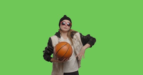 Girl wearing street hip hop style posing over green screen background. Young woman holding basketball ball on Chroma Key. 4k raw video footage slow motion 60 fps