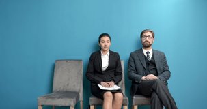 Portrait of male and female candidates with resume sitting in waiting room with classic blue walls. Two people in formal clothing waiting in queue for job interview.