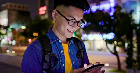 asian young man use smart phone while walking outdoor in the dark