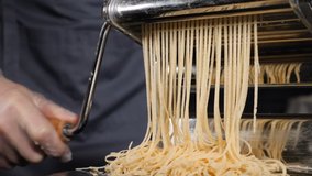 Traditional italian homemade pasta being made on machine for cutting dough. Slow motion food footage of Fresh spaghetti pasta coming out of pasta machine, close-up. Chef use pasta cutting machine