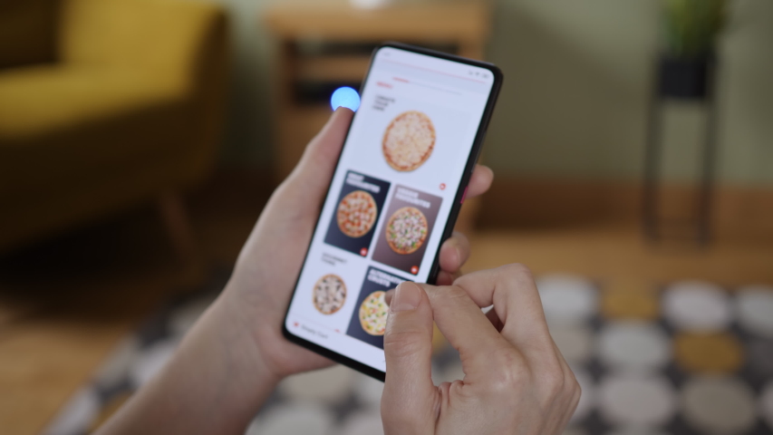 Orders Pizza Using Online Delivery. Woman Orders Food Home In Online Store Using a Smartphone. Female Ordering pizza using food delivery app. Woman at Home Lying on Couch in Living Room Smartphone. | Shutterstock HD Video #1047443878