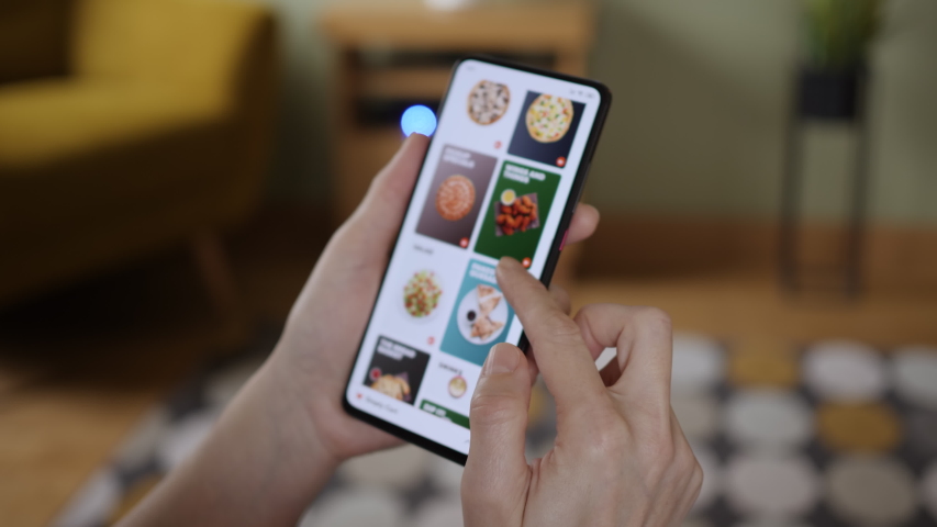 Orders Pizza Using Online Delivery. Woman Orders Food Home In Online Store Using a Smartphone. Female Ordering pizza using food delivery app. Woman at Home Lying on Couch in Living Room Smartphone. Royalty-Free Stock Footage #1047443878