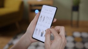 Woman Looks at Goods in Online Store Clothing. Buy Fashion Clothes Directly on Smartphone. Woman at Home Lying on Couch in Living Room Using Smartphone Buys in Internet Shop.