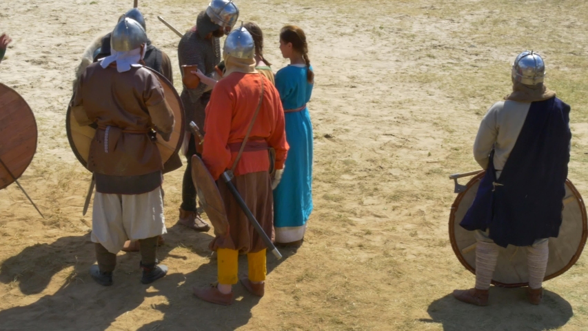 Knights in armor, with shields and swords on the battlefield, drink water from the jug that the girl brought them. Ready to fight the enemy.