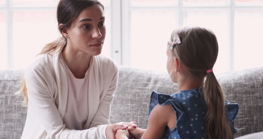 Caring young mom holding hands talking to small child girl. Foster care parent comforting helping adopted kid give care and protection. Loving mum and small daughter having trust conversation at home Royalty-Free Stock Footage #1047458557