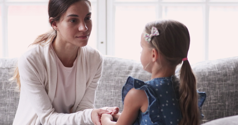 Caring young mom holding hands talking to small child girl. Foster care parent comforting helping adopted kid give care and protection. Loving mum and small daughter having trust conversation at home | Shutterstock HD Video #1047458557
