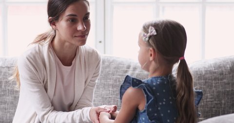 Caring young mom holding hands talking to small child girl. Foster care parent comforting helping adopted kid give care and protection. Loving mum and small daughter having trust conversation at home
