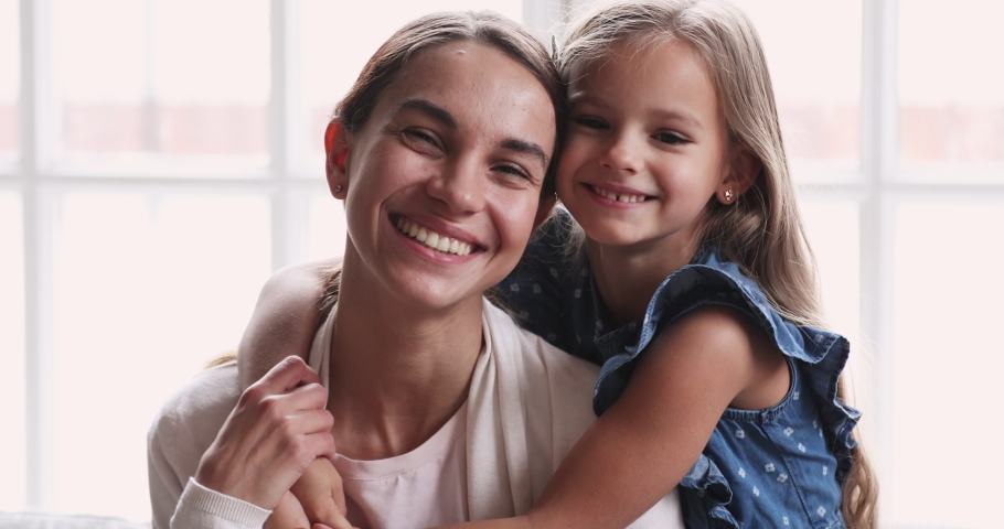 Pretty smiling child daughter embrace mom look at camera. Happy beautiful family young adult single mother foster parent and cute kid girl hug cuddle enjoy sweet tender love concept. Close up portrait Royalty-Free Stock Footage #1047458596