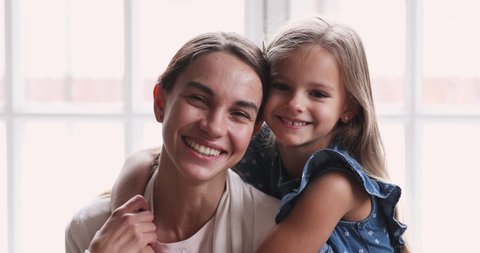 Pretty smiling child daughter embrace mom look at camera. Happy beautiful family young adult single mother foster parent and cute kid girl hug cuddle enjoy sweet tender love concept. Close up portrait