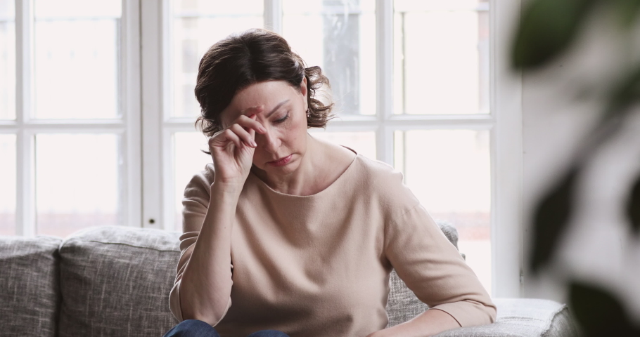 Sad middle aged woman sit alone feel depressed lonely. Upset mature single lady thinking of health problem divorce solitude. 50 year old female suffer from melancholy loneliness mental disorder | Shutterstock HD Video #1047458611
