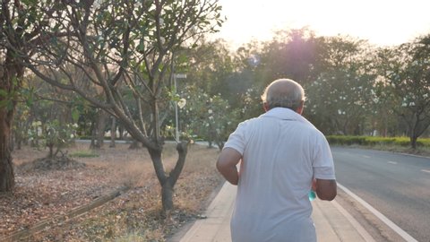 Rear view Asian elderly exercise. Senior man running on road in public park that has sunshine in the evening. health lifestyle and exercise Concept. Slow Motion