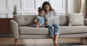 Full length excited smiling young mommy hugging small preschool girl. listening to favorite music cartoons sound track on laptop. relaxing on sofa, enjoying leisure time together in living room.