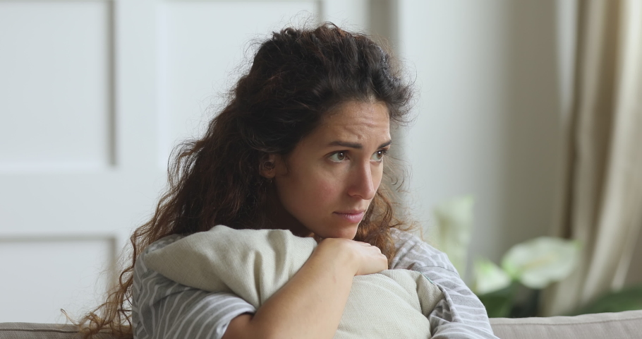 Nervous young woman embracing pillow, feeling unsure about hard decision, sitting alone on sofa. Depressed lady regretting mistake abortion, suffering from psychological problem trouble at home. | Shutterstock HD Video #1047476635