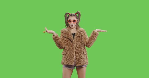 Fashion girl wearing leopard fur coat licking candy. Freak young sexy woman with lollipop having fun . Vogue style female dancing over green screen background chroma key