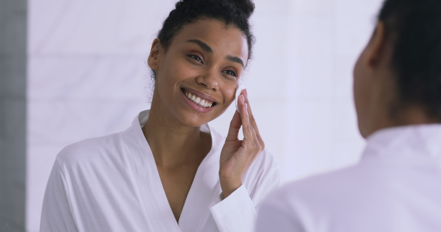 Focused young african american woman applying toner, feeling excited with skin condition. Happy millennial biracial girl using cotton disposable pads, clean moisturize skin before starting makeup. Royalty-Free Stock Footage #1047481861