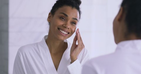 Focused young african american woman applying toner, feeling excited with skin condition. Happy millennial biracial girl using cotton disposable pads, clean moisturize skin before starting makeup.