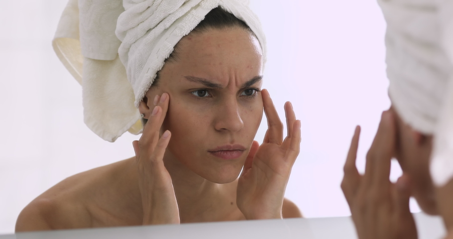 Frustrated young mixed race girl with towel on head looking at mirror, worrying about first wrinkles. Unhappy woman dissatisfied with skincare product effects or skin condition, feeling stressed. Royalty-Free Stock Footage #1047481864
