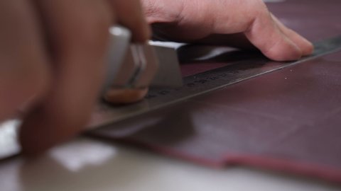 Close-up shot of craft master cutting leather with utility knife. Handmade and leatherwork concept. Manufacturing leather process in small private factory. bag and wallet handmade making. 4 k footage
