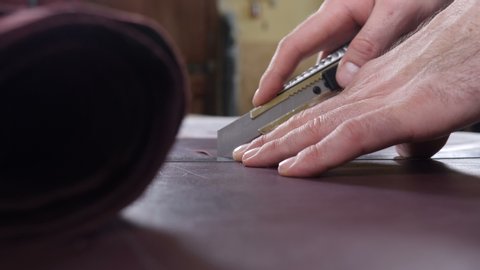 Close-up shot of craft master cutting leather with utility knife. Handmade and leatherwork concept. Manufacturing leather process in small private factory. bag and wallet handmade making. 4 k footage