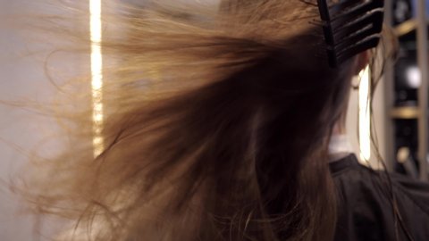 Drying with a hair dryer in the hairdresser's salon. View of the girl from behind. Hair flies into the camera. Slow motion 4K 50fps