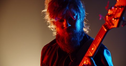 A cool grunge rock musician is performing on stage of club, making an amazing solo on his bass guitar, lit by red and blue neon lights - music concept 4k footage