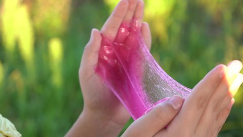 Closeup view 4k video of two kids hands holding pink transparent slime, squeezing and pulling it. 