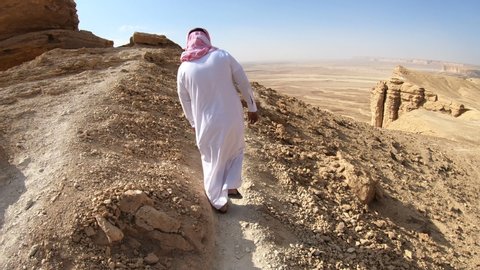 EDGE OF THE WORLD, SAUDI ARABIA – DECEMBER 2019: Following a tour guide wearing traditional dress walking on steep mountain path at the Edge of the World in Saudi Arabia